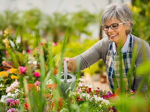 Active Adult woman watering flowers in her courtyard>